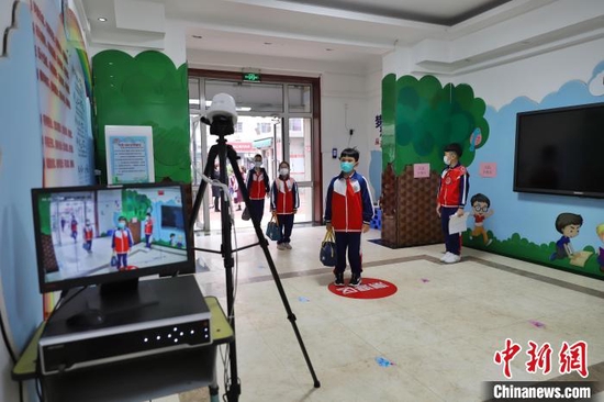 天津中小学今日恢复线下教学，图为天津市和平区万全第二小学的学生在进行第一次测温后进入学校王在御摄