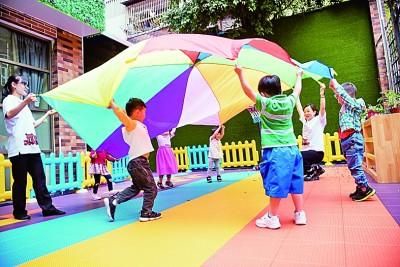 广州，一托育中心的老师和孩子们正在玩“彩虹伞”游戏。光明图片